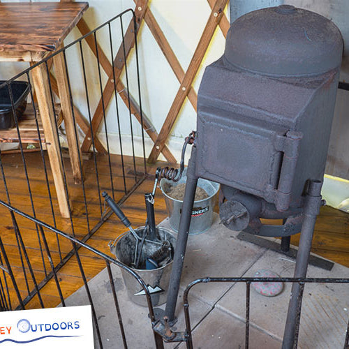 Vintage-style stove or furnace on a stand with a wooden floor and furniture in the background.